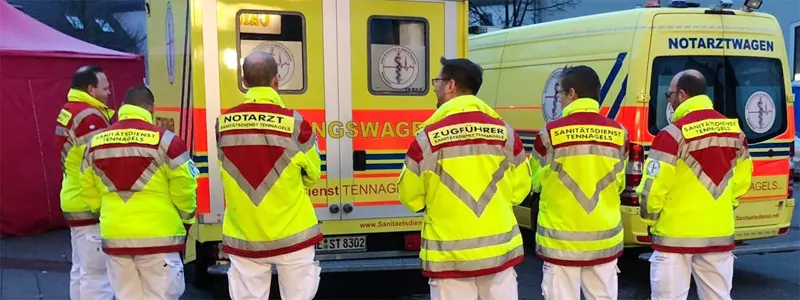 Einsatzkräfte des Sanitätsdienst Tennagels in Einsatzjacken vor einem Rettungswagen und einem Notarztwagen